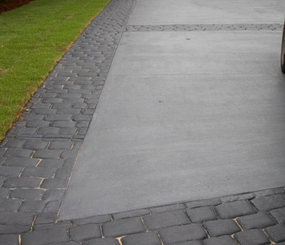 Worn and weathered stone look decorative concrete edging around a plain gray concrete driveway.