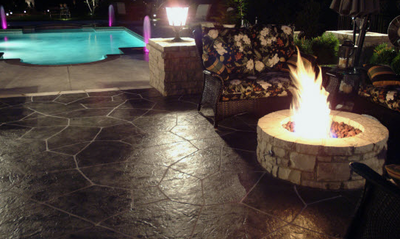 Dark colored stain and stamped in a stone design with a built in fire pit next to a built in pool.